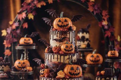 Ornate tiered Halloween cake with chocolate bats, jack-o'-lanterns, and fall leaves in a festive dessert display.